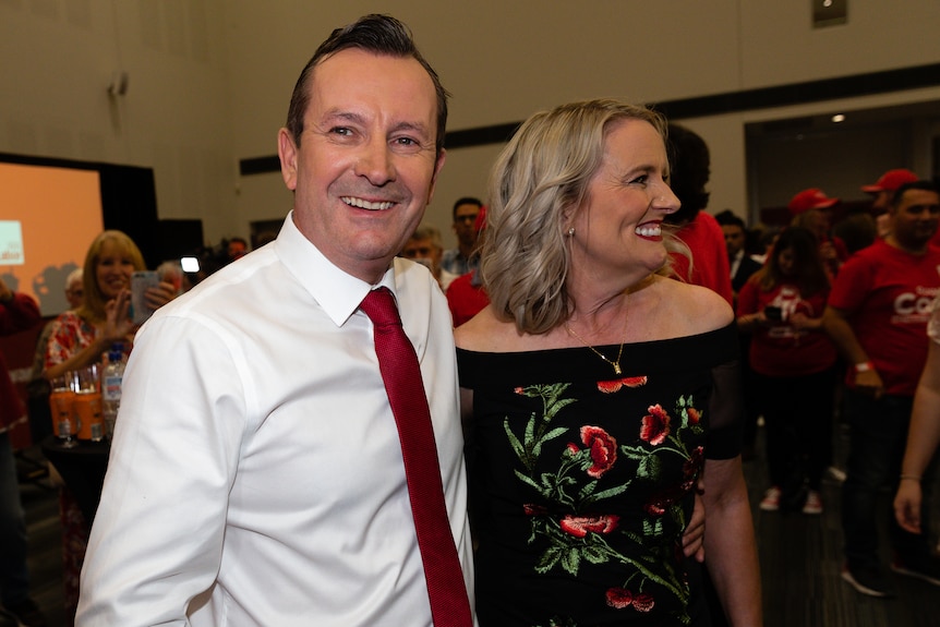 A man wearing a shirt and tie standing next to a woman in an off-the-shoulder dress.