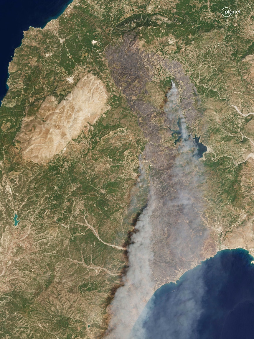 A satellite image of fire and smoke drifting across an island 