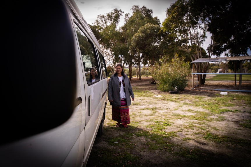 A woman stands on grass near a mini bus. 