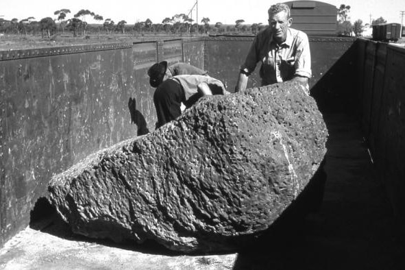 A black and white photo of three men behind a large meteorite sitting in a rail carriage.