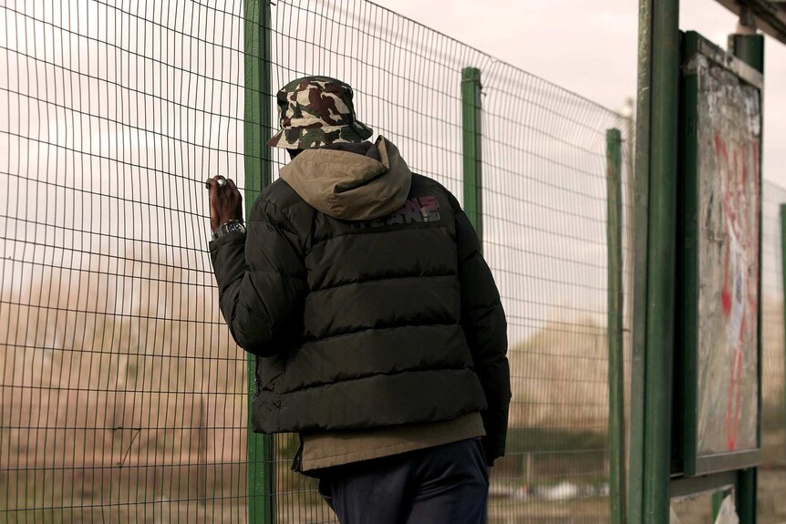 A man looks through a fence.