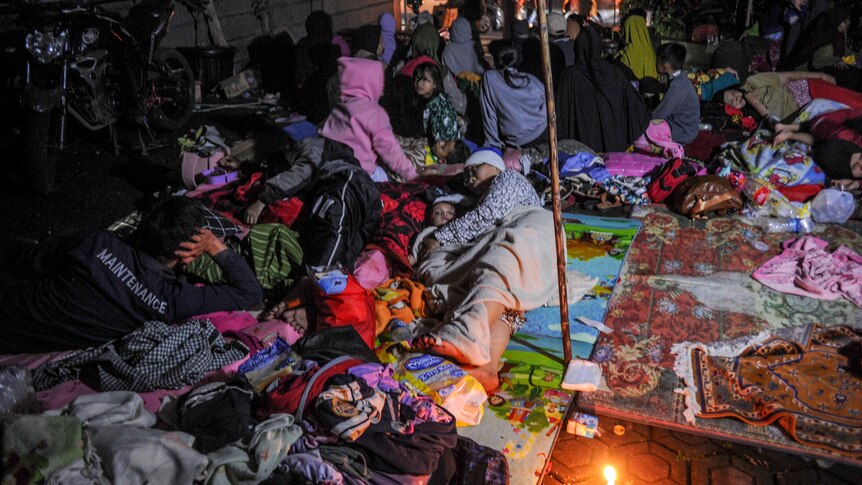 Women and children sleep on blankets on the ground under tarps. 