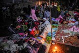 Women and children sleep on blankets on the ground under tarps. 