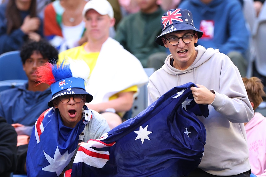 Two tennis fans, in stands, holding Australian flags and wearing Australian flag hats, cheering