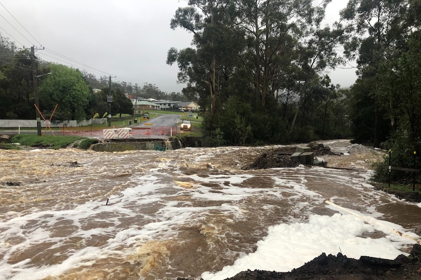 Water gushes over a road where a bridge was washed away