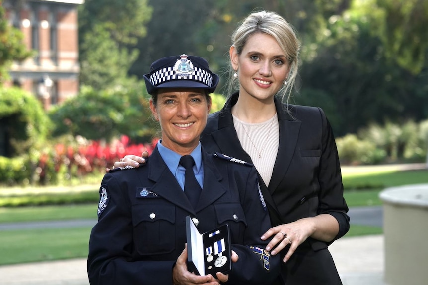 A police officer holding a medal stands next to a young woman
