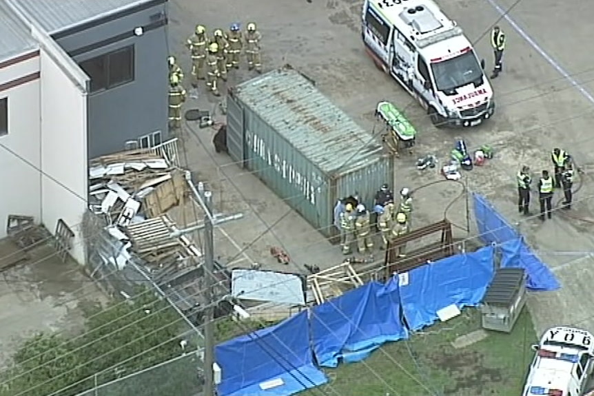 An aerial shot of paramedics, police and firefighters standing around a shipping container which has had a hole cut in one end.