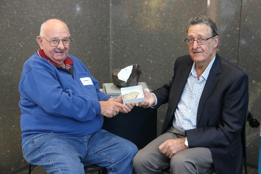 Two men sit on either side of a meteorite.