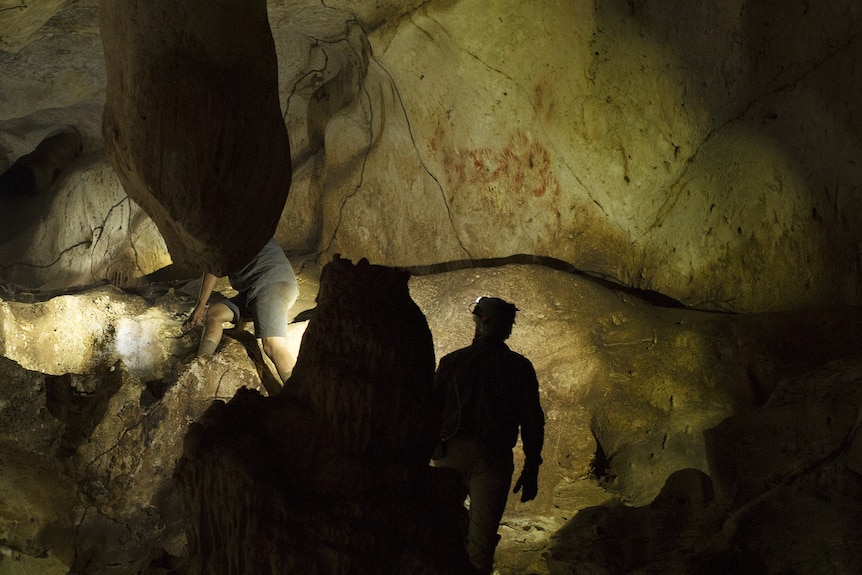 Two men in a cave with hand stencil art on the walls