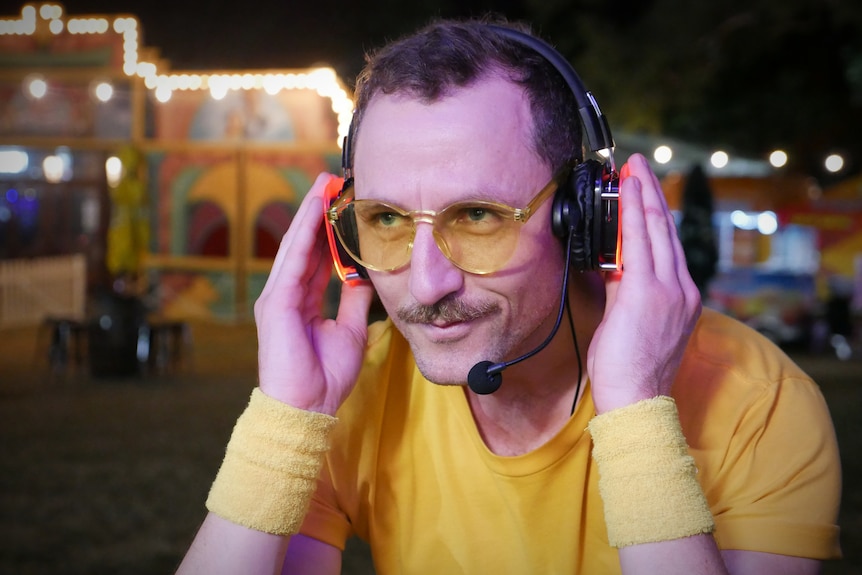 A man in yellow sunglasses and sweatbands wearing a set of headphones.
