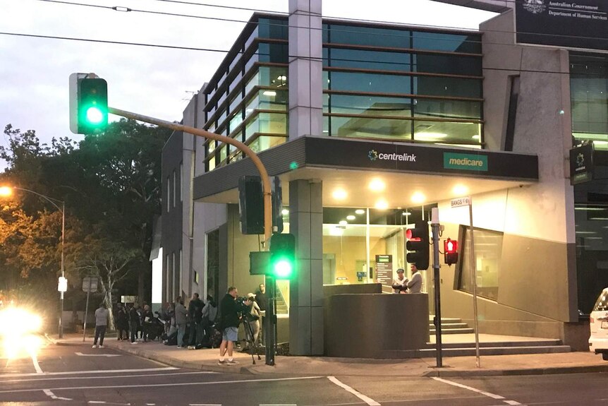 A queue of people line up at sunrise outside a Centrelink building.