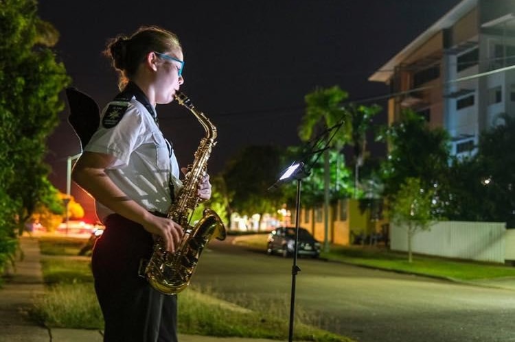 Very early-morning shot of young girl in a ambulance cadet uniform playing sax reading music from phone on a music stand.
