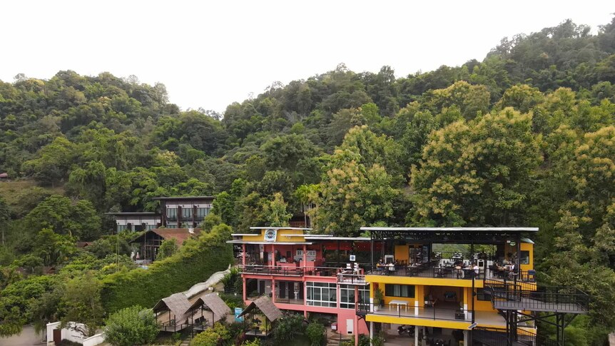 A colourful restaurant nestled into a background of green trees with little huts sitting out front.