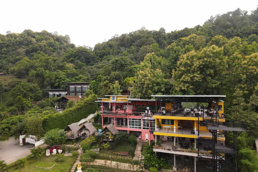 A colourful restaurant nestled into a background of green trees with little huts sitting out front.