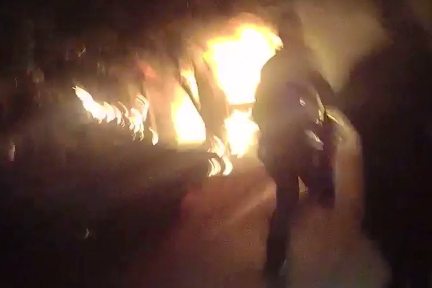 A grainy image of police officers running towards a burning house.