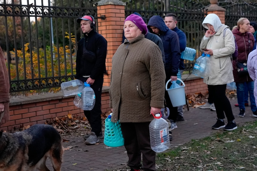 People lining up holding water bottles and containers in hands. 