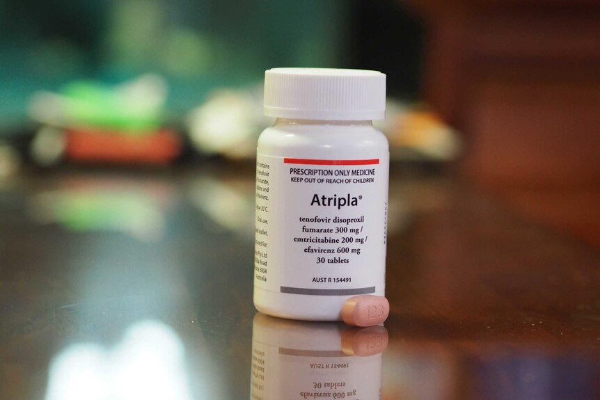 A small pill sits next to a container on a bench. The label says 'Atripla', which is an antiviral medication that treats HIV.