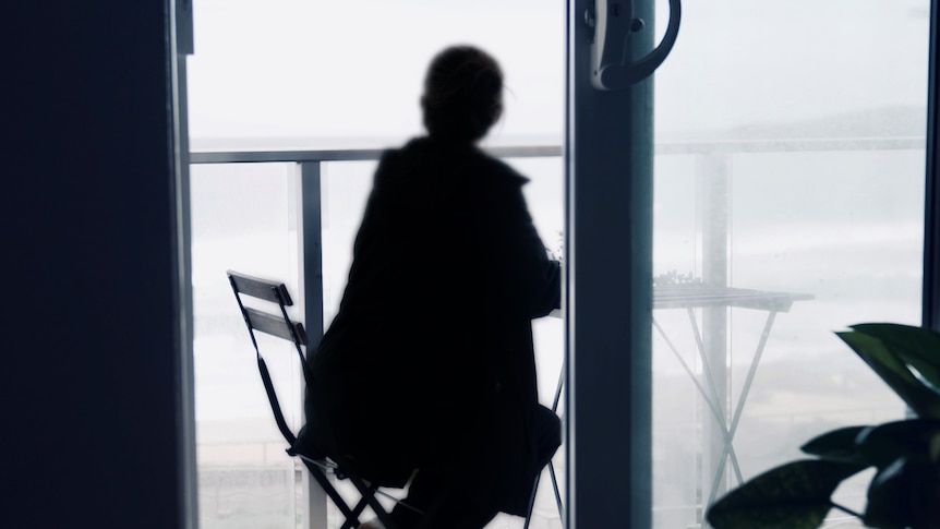 Woman sitting on a balcony, facing away to the ocean.