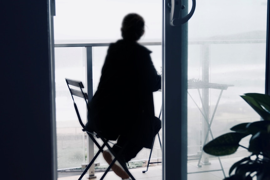 Woman sitting on a balcony, facing away to the ocean.