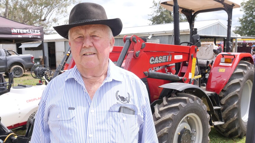 A man wearing a broad brimmed hat and standing in front of a tractor 