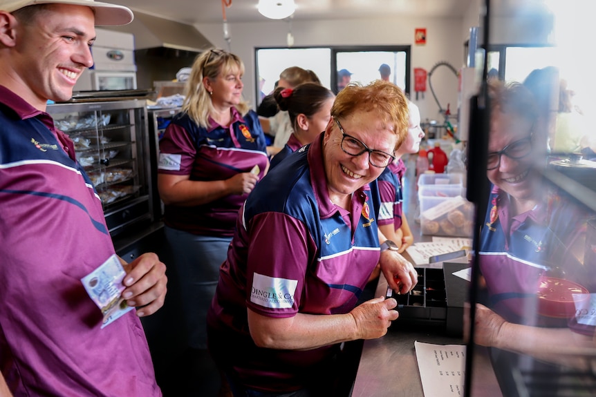 Woman with red hair smiling while at cash register inside canteen with other similarly dressed volunteers around her