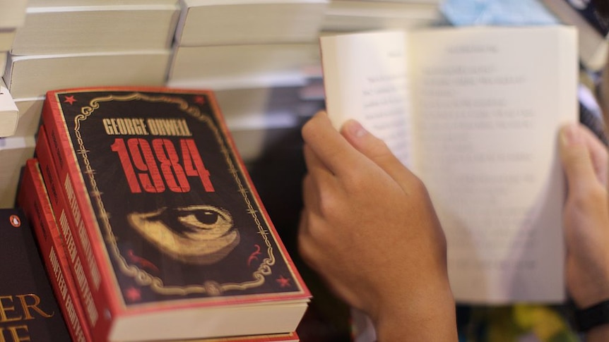 A pile of 1984 books, one is is held by a boy