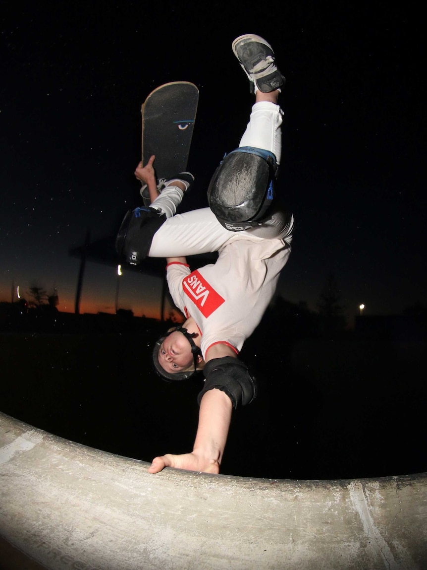 Skater pictured at night performing a trick upside down supported by one hand.