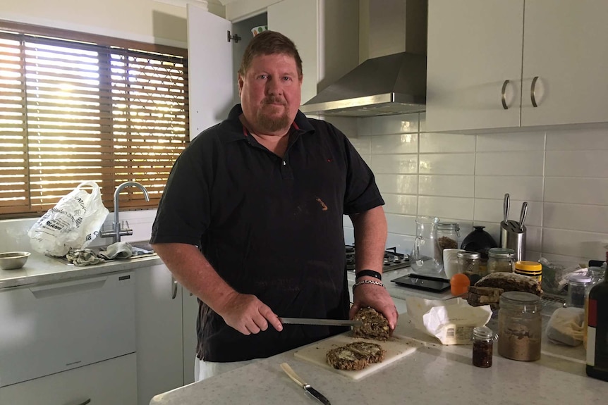 Gary Fitzgerald is standing at his kitchen bench buttering bread.