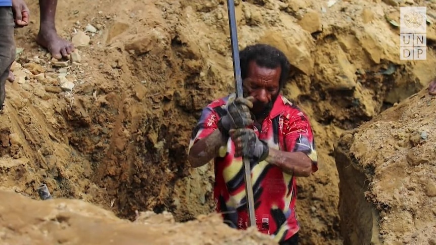 A man digs with a metal pole through earth and mud.