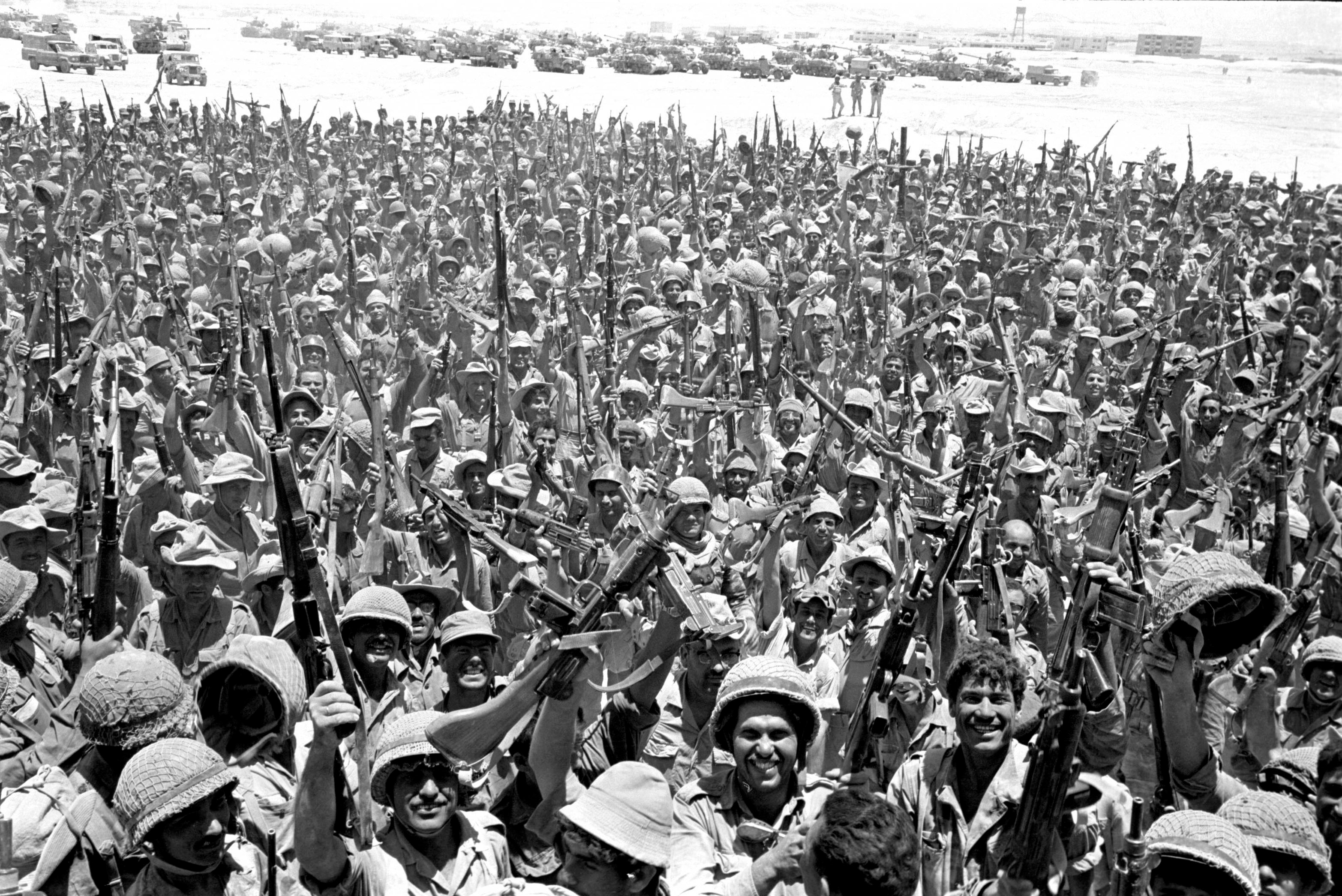 A black and white photo of countless soldiers celebrating in the desert.