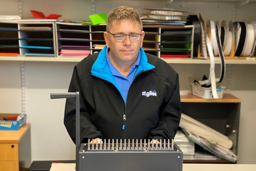 A man in a jacket stands in front of a binding machine in a stationery room