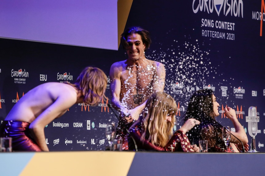 A couple of band members duck as the lead singer sprays champagne at the press conference after winning Eurovision. 