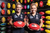 Two identical twin sisters hold footballs in their Carlton gear ahead in 2019 AFLW grand final week.