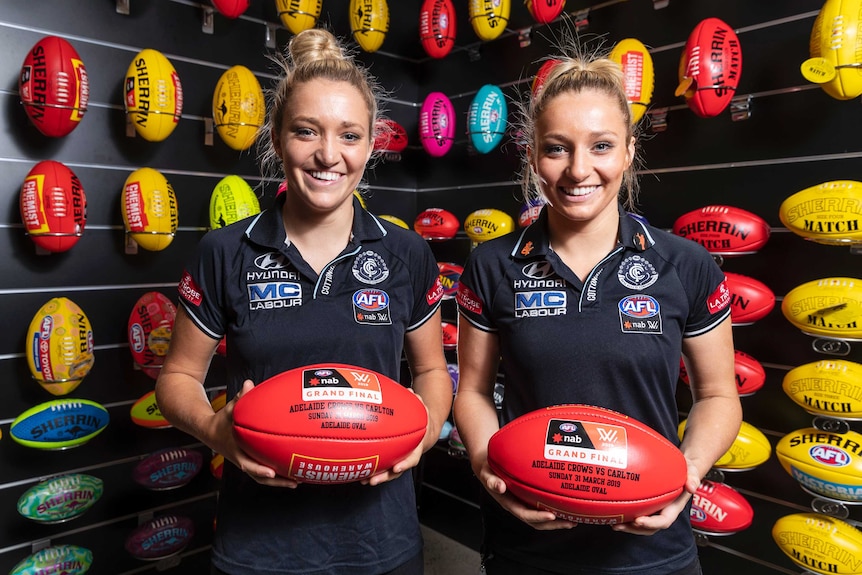 Two identical twin sisters hold footballs in their Carlton gear ahead of 2019 AFLW grand final week.