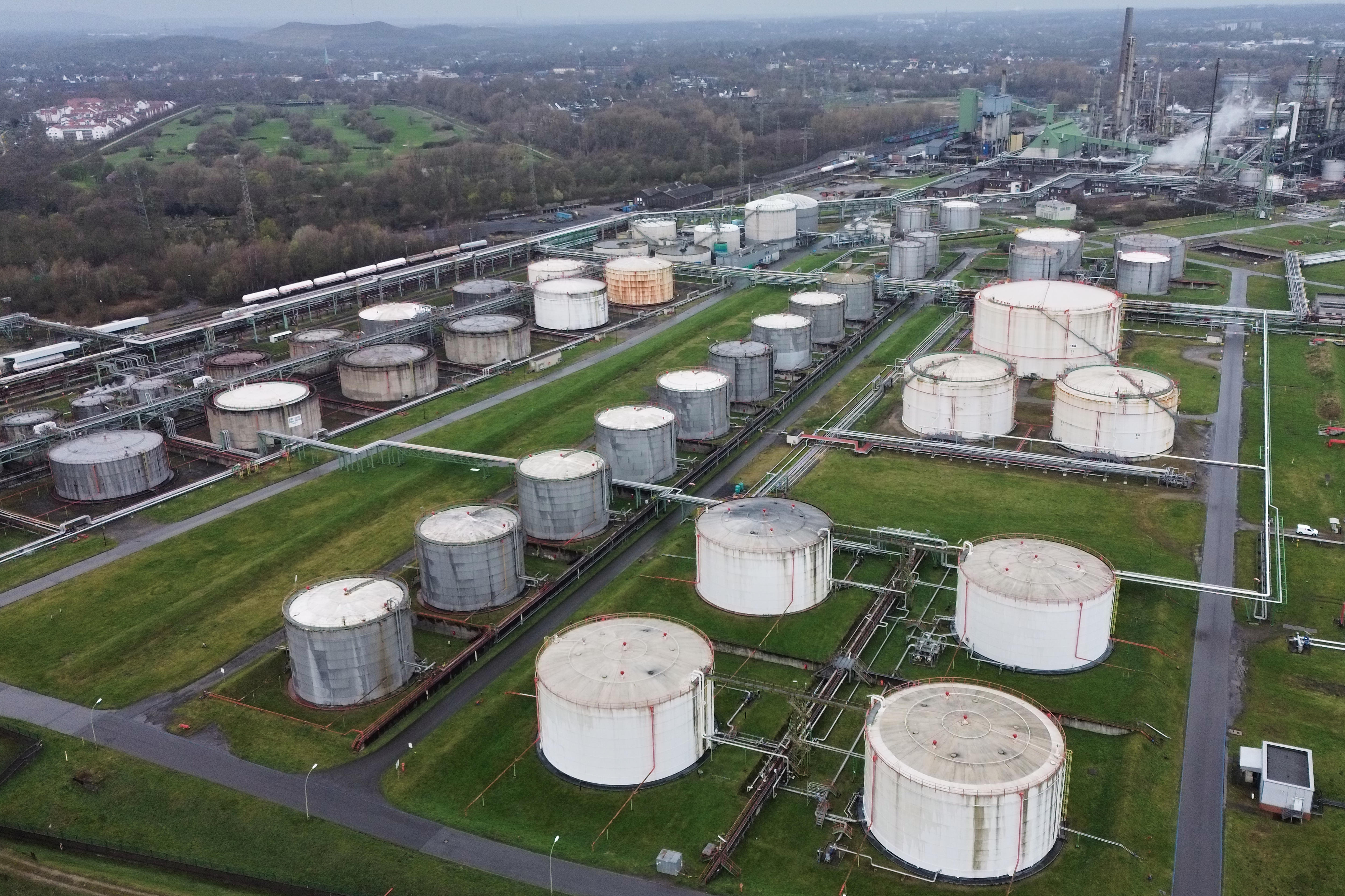 Rows of white oil tanks are seen outdoors in front of a refinery. 