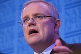 Low angle looking up at Scott Morrison speaking at a podium.