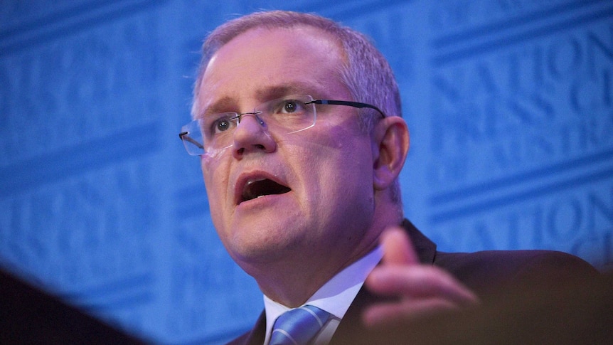 Low angle looking up at Scott Morrison speaking at a podium.