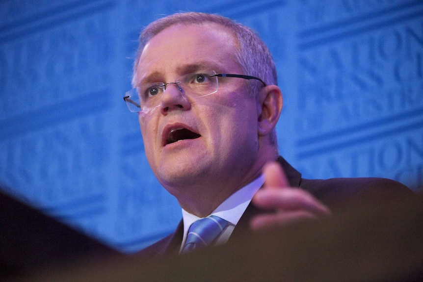 Low angle looking up at Scott Morrison speaking at a podium.