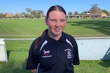 A teenage girl standing in front of an Australian Rules football field