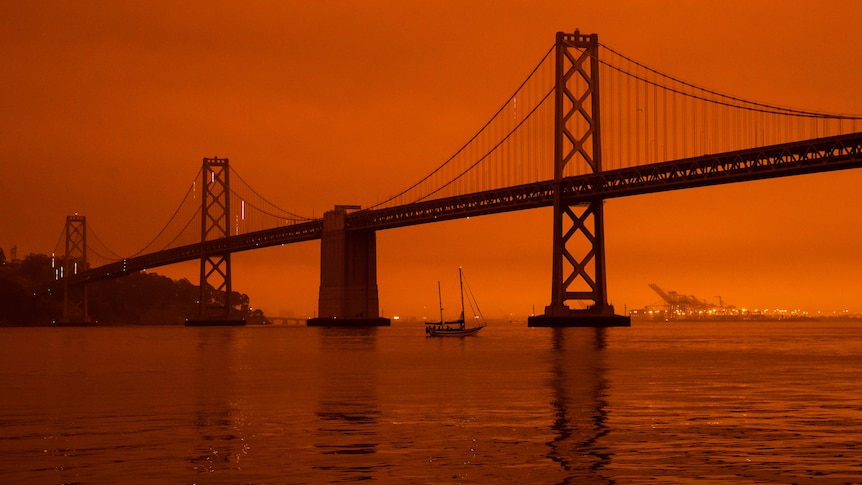 A large suspension bridge and water with a boat is covered in a smoky, orange glow