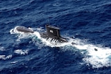 An aerial photo shows a submarine breaking the waterline on a clear day in deep blue waters.