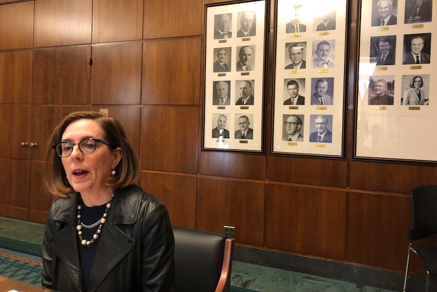Oregon Governor Kate Brown speaks to reporters in front of pictures of previous state governors in Salem.