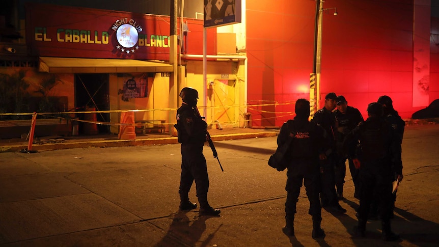 Several police officers with guns patrol a the Caballo Blanco bar, which is taped off.