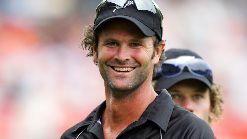 Chris Cairns smiles at the camera wearing black cricket kit