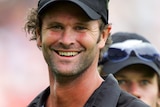 Chris Cairns smiles at the camera wearing black cricket kit