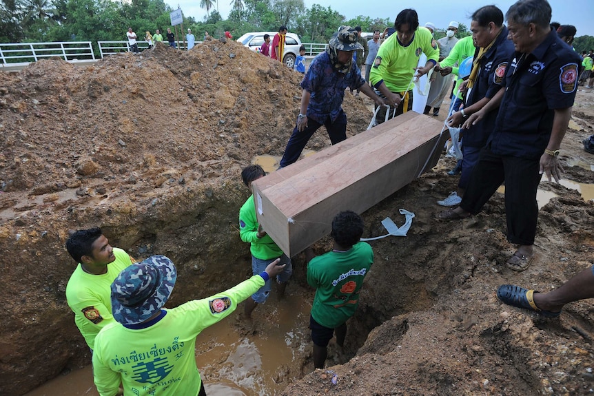 Rescue workers bury coffins containing the human remains of migrants found in Thailand