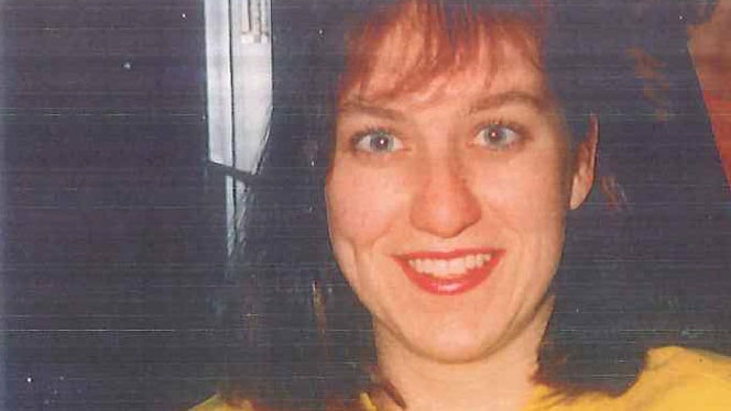 Missing woman Julie Cutler holds up a drink. She wears a bright yellow jumper and is smiling.