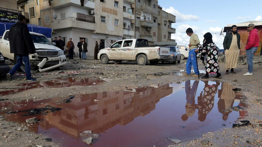 People walk near a puddle of water mixed with blood at the site of twin car bombs in Benghazi.