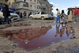 People walk near a puddle of water mixed with blood at the site of twin car bombs in Benghazi.