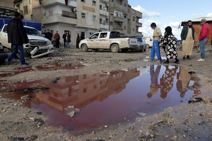 People walk near a puddle of water mixed with blood at the site of twin car bombs in Benghazi.